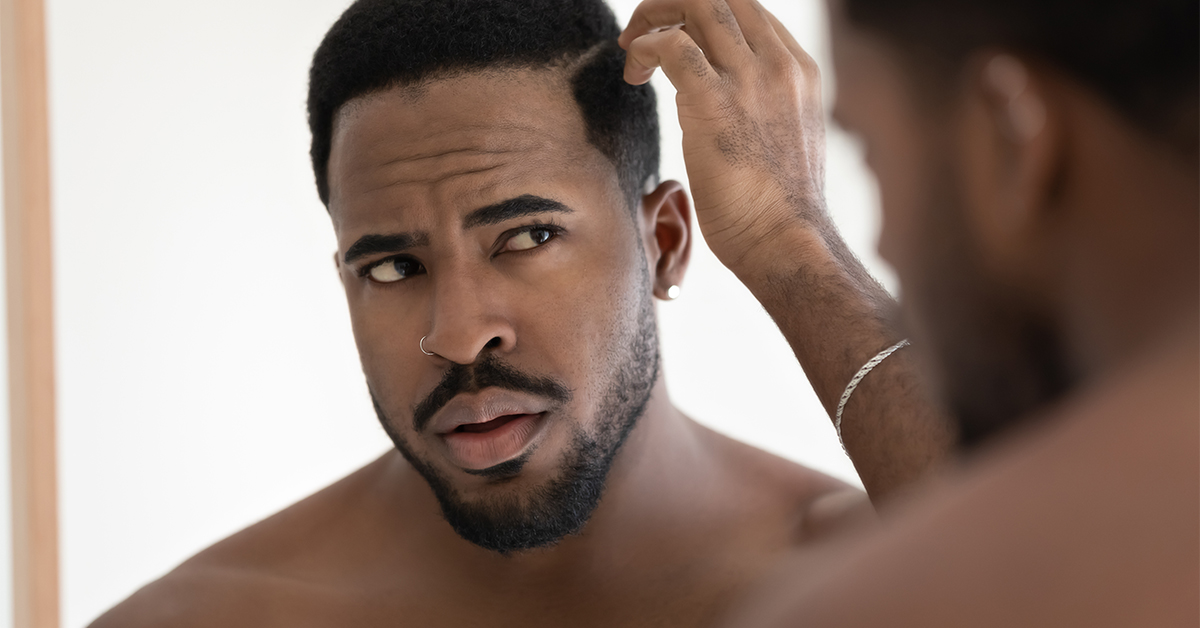 Black man checking hair line for thinning.