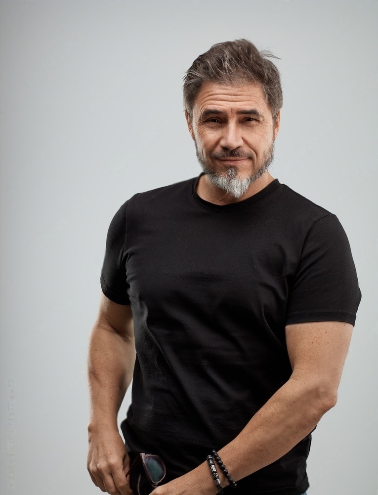 Middle-aged man with a beard wearing a black t-shirt, standing confidently against a light backdrop. Suitable for a personal branding context.