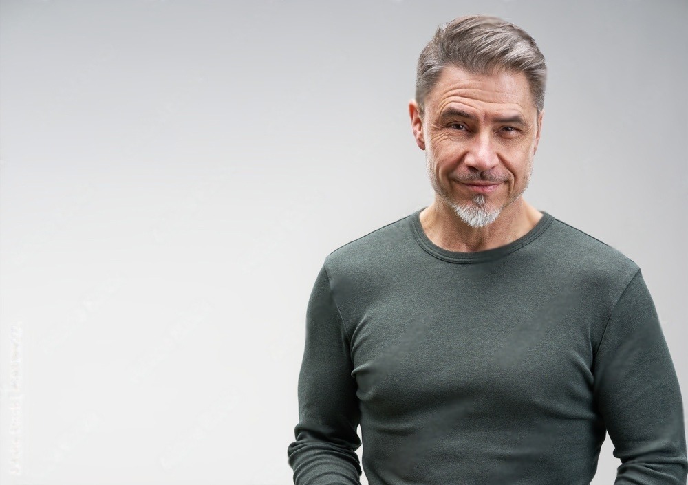 Confident middle-aged man with short gray hair and a goatee, wearing a fitted dark green shirt. The expression conveys warmth and approachability.