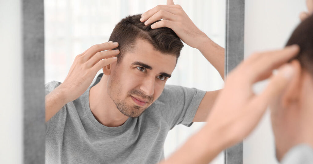 A young man inspects his hairstyle in a mirror, adjusting his hair while considering his appearance. The image emphasizes grooming and self-care.