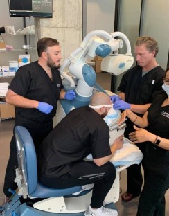 Dental professionals assist a patient during a procedure at a clinic. The setting is modern, showcasing advanced dental equipment and teamwork.