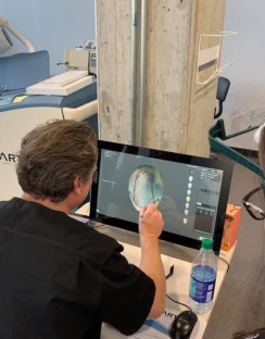 A healthcare professional interacts with a touchscreen monitor displaying a 3D brain model, engaged in detailed analysis during a medical examination.