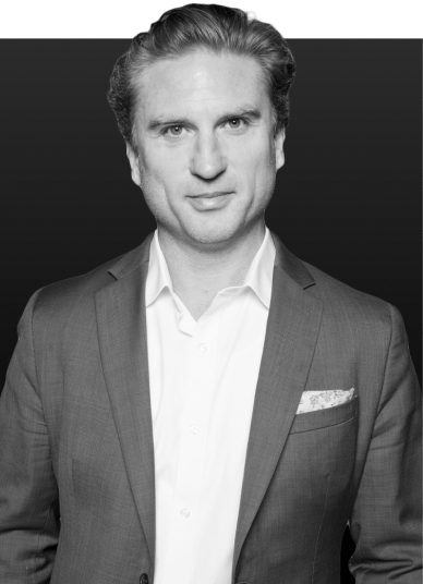 Man in a tailored gray suit with a white shirt and pocket square, posing confidently against a dark background. Suitable for professional profiles or business contexts.